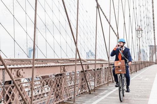 USA, New York City, man on bicycle on Brooklyn Bridge using cell phone photo