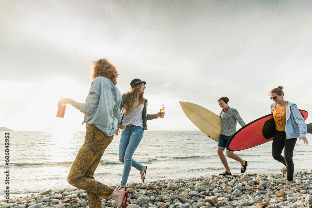 Happy friends with surfboards walking on stony beach - obrazy, fototapety, plakaty 