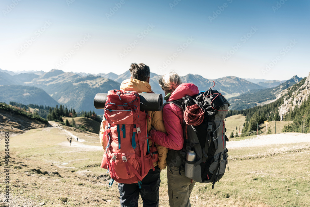 Austria, Tyrol, rear view of couple on a hiking trip in the mountains enjoying the view - obrazy, fototapety, plakaty 