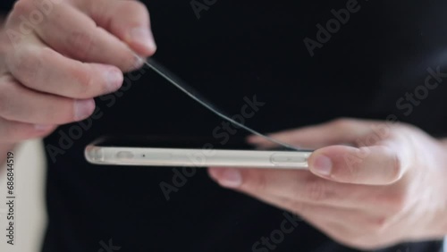 Unrecognisable repairman is removing cracked broken and old tempered glass screen protector from smartphone, close up view. Services for gluing and replacement of damaged protective glass photo
