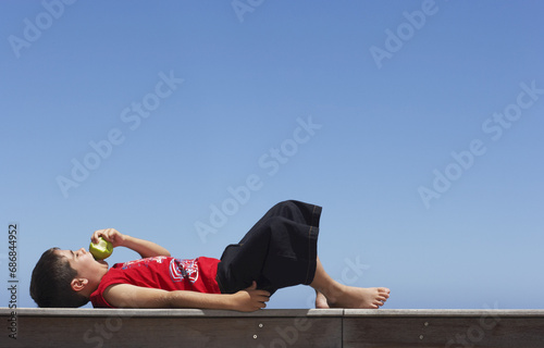 Boy Lying Down Outdoors, Eating Apple photo