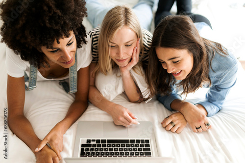 Three girlfriends lying on bed sharing laptop photo