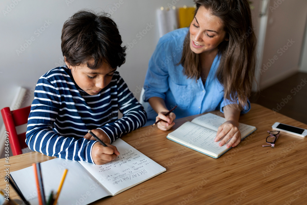Young woman assisting boy in writing homework on table at home Young woman assisting boy in writing homework on table at home