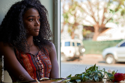Portrait of young African woman with flowers on the table in a cafe, looking out of window photo