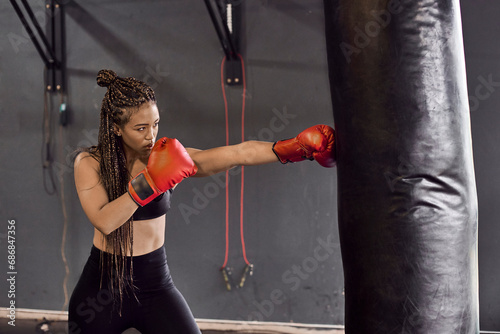 Female boxer wearing red gloves practicing boxing drill on punching bag in gym photo