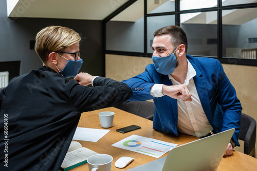 Male and female entrepreneurs wearing masks while greeting with elbow bump in board room during coronavirus pandemic photo