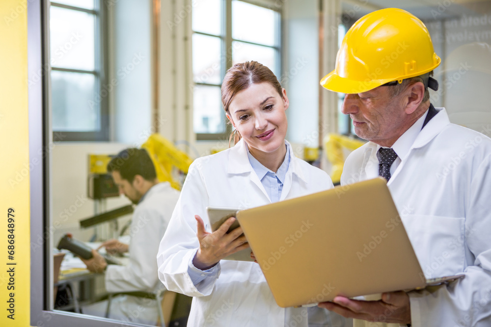 Two engineers in factory with tablet and laptop Two engineers in factory with tablet and laptop