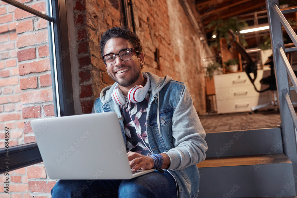Young man with earphones sitting on office stairs, using laptop Young man with earphones sitting on office stairs, using laptop