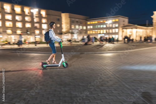 Young woman riding an electric scooter on 'Pariser Platz' at night, Berlin, Germany photo