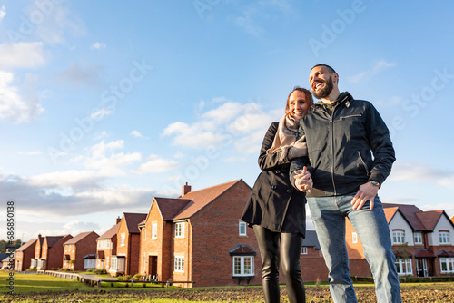 Happy couple looking away while standing outside newly built houses against sky