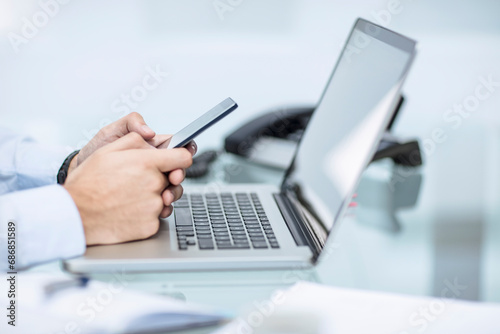 Businessman using smart phone at desk with laptop photo