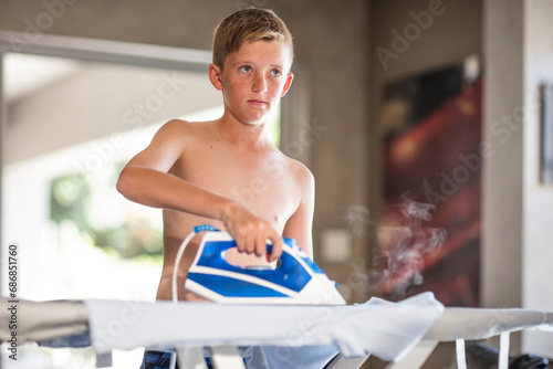 Shirtless teenage boy ironing cothes at home photo
