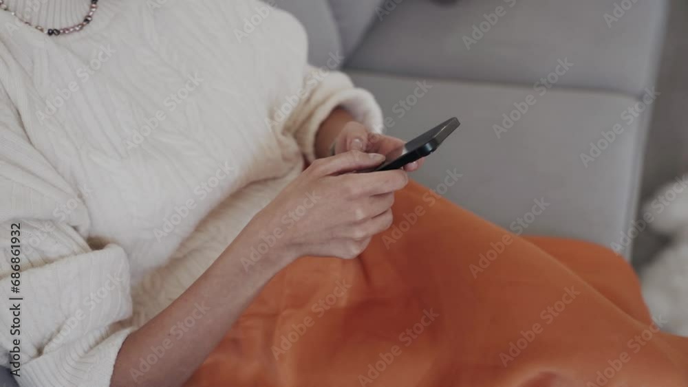 Crop faceless woman using smartphone while sitting on sofa at home Crop faceless woman using smartphone while sitting on sofa at home