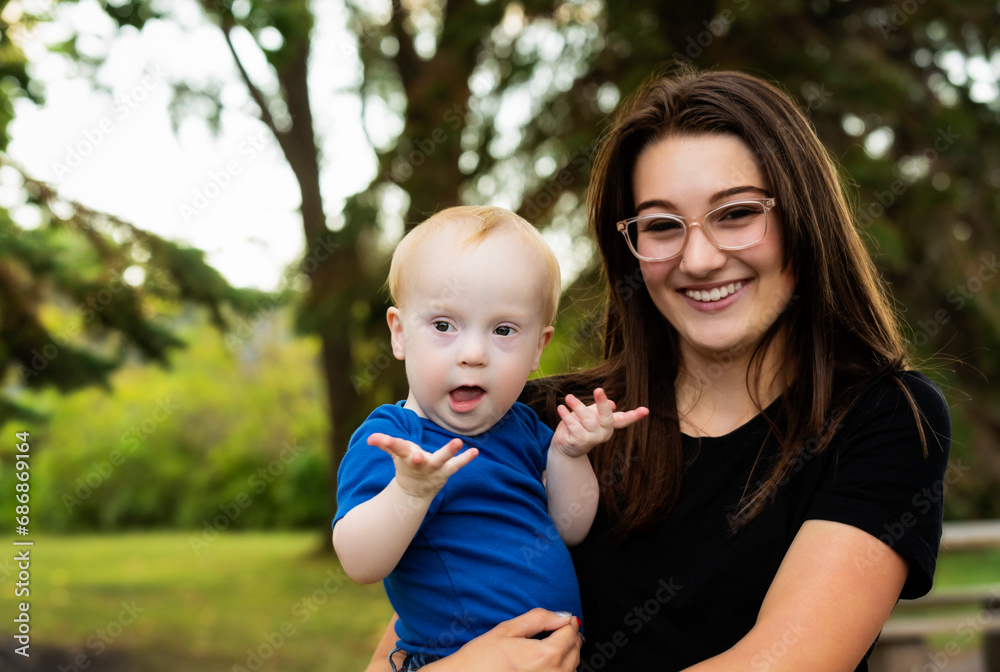Outdoor portrait of an older sister spending quality time with her young brother who has Down Syndrome, in a city park during a warm fall afternoon; Leduc, Alberta, Canada Outdoor portrait of an older sister spending quality time with her young brother who has Down Syndrome, in a city park during a warm fall afternoon; Leduc, Alberta, Canada