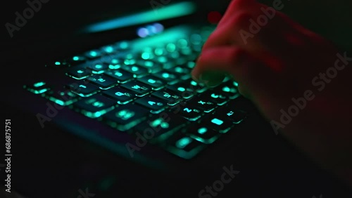 Close up view of unrecognizable person's hand playing video game on a laptop with a black keyboard with multicolored neon backlit. Focus on WSAD, SHIFT keys. photo