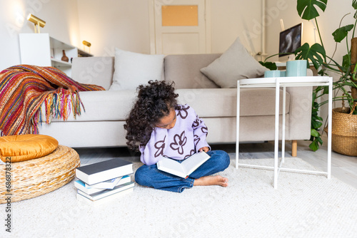 POC girl sitting on carpet infront of sofa reading a book photo