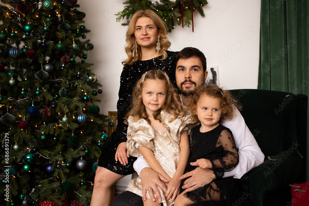 portrait of father, mother and girls sister smile on a background of Christmas trees in the interior of the house portrait of father, mother and girls sister smile on a background of Christmas trees in the interior of the house