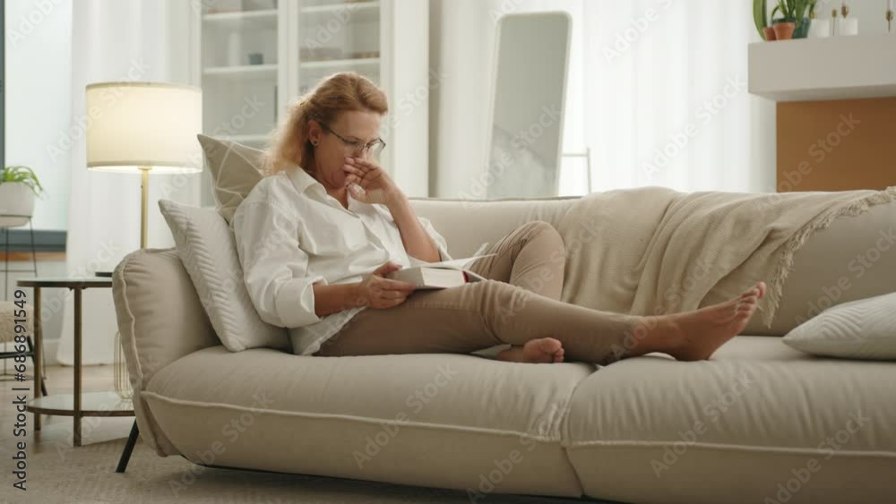 Nice mature blonde in glasses yawning, putting book aside on sofa, turning to her side, closing eyes and peacefuly falling asleep at daytime in modern flat. High quality 4k footage Nice mature blonde in glasses yawning, putting book aside on sofa, turning to her side, closing eyes and peacefuly falling asleep at daytime in modern flat. High quality 4k footage