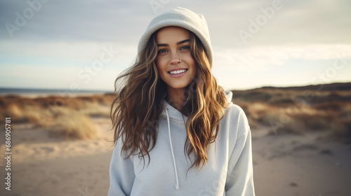 smiling woman with long, curly hair on beach, wearing white hoodie. captures leisure and enjoyment in a relaxed, picturesque setting. © wetzkaz