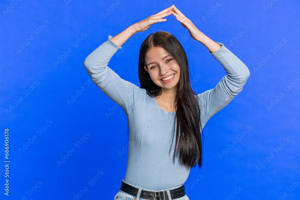 House roof about head. Happy woman playing childish catching up game, feeling in safe making roof above head with hands, insurance, security service. Smiling girl isolated on blue studio background House roof about head. Happy woman playing childish catching up game, feeling in safe making roof above head with hands, insurance, security service. Smiling girl isolated on blue studio background