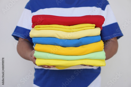 Close up man holds stack of colorful folded clothes after doing laundry. Concept, daily chore, household. Folded clothes for neat and clean. Maintenance and keep garments for sanitary. 