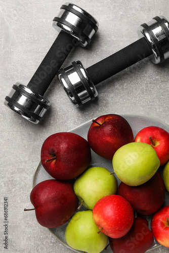 Healthy diet. Plate with apples and dumbbells on light grey textured table, flat lay