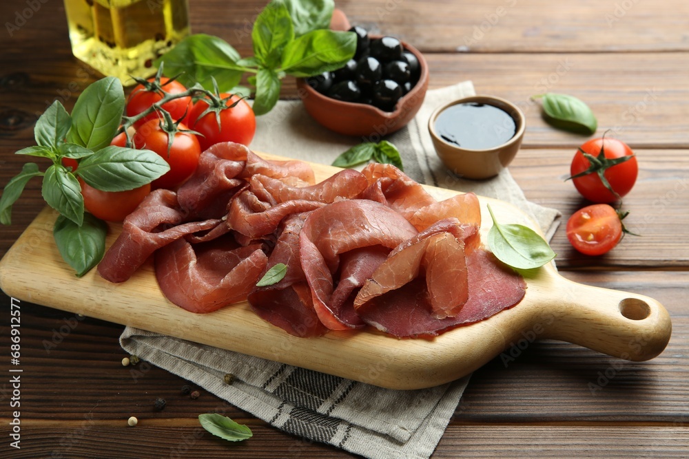 Board with delicious bresaola served with other snacks on wooden table