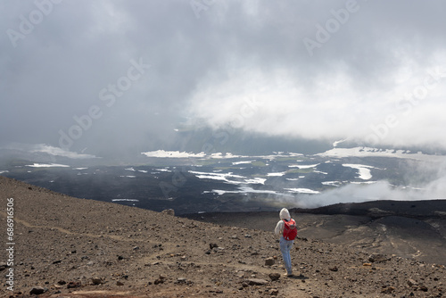 A girl with a backpack walks along the slope of the volcano. Low clouds. Travel, tourism and hiking on the Kamchatka Peninsula. Nature of the Russian Far East. Gorely volcano, Kamchatka Krai, Russia. photo