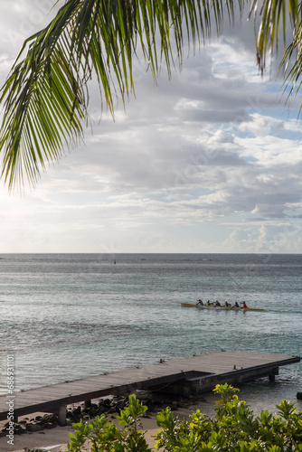 Traditional Tahitian rowers over the ocean rowing a boat at sunset with a palm tree