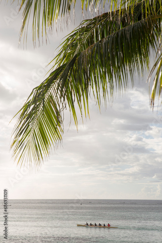 Traditional Tahitian rowers over the ocean rowing a boat at sunset with a palm tree