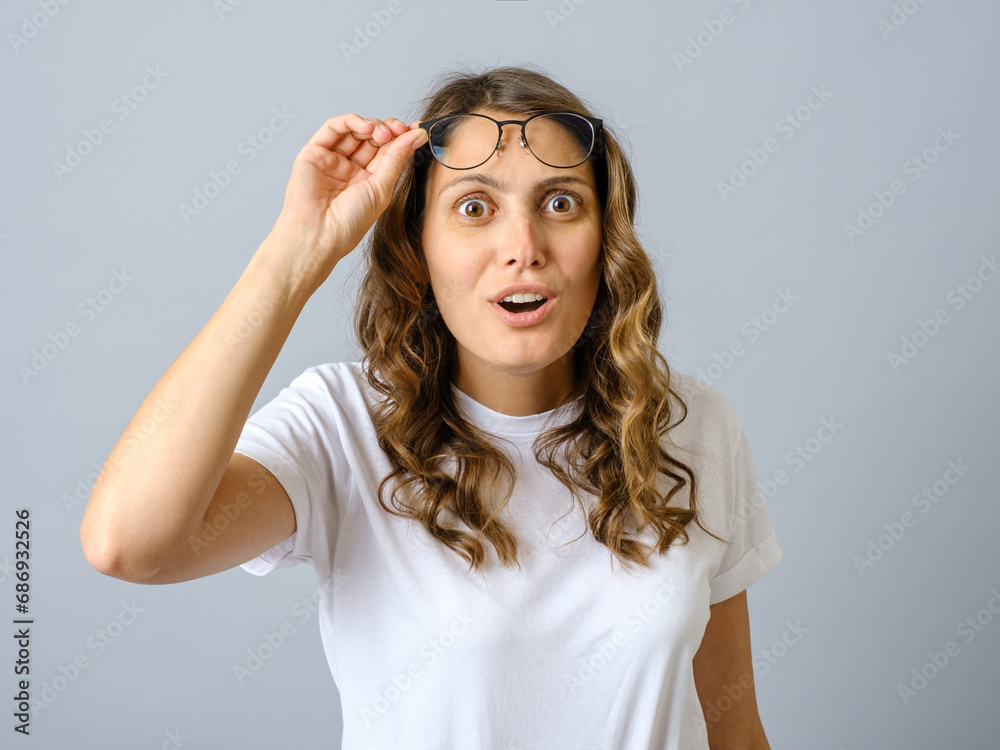Photo of surprised cheerful woman looks wondered through spectacles cannot believe her eyes