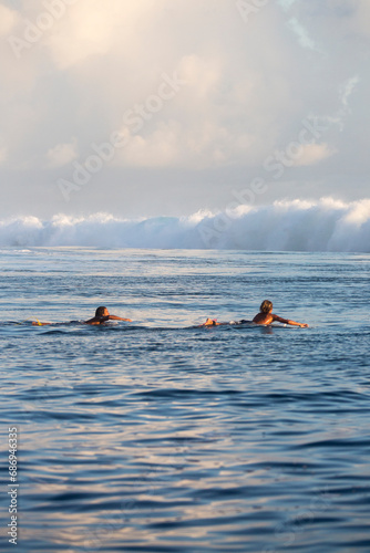 Surfers at sunset wait to catch a wave in Tahiti 