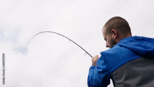 Fisherman with fishing rod or spinning and professional tools sitting on the river bank rear view Pull fish out of the lake sports fishing photo