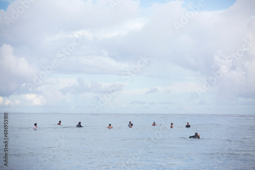 Surfers wait in the water with their backs turned to camera in Tahiti on the ocean