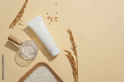 Rice, rice bran and an unlabeled white tube are placed on a beige background. Empty space for text design. Skin care with vegan cosmetics-safety for skin.