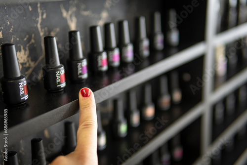 choice of nail polish. A finger with a red-painted fingernail points at the bottles of nail polish. lots of nail polish options on the shelf in the store. photo