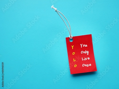 On blue copy space background, red tag with text written You Only Live Once - concept of YOLO - ideology is an encouragement to seize the day, to go for it, live your best life now