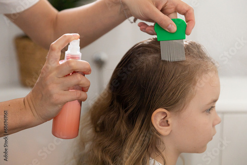 A woman helps to get rid of lice and parasites on the head of a little girl, combs her head with a special comb and and shampoo. Treatment of lice and nits