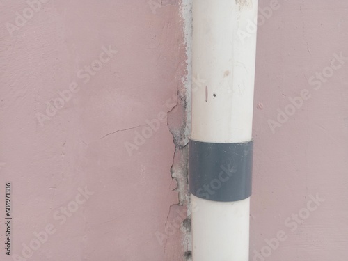 White pvc pipe clamped on a faded pink wall. suitable for texture and background themes.