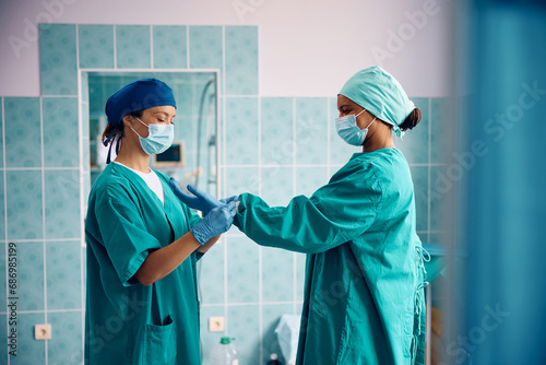 Black female doctor preparing for surgery with help of nurse in operating room. photo