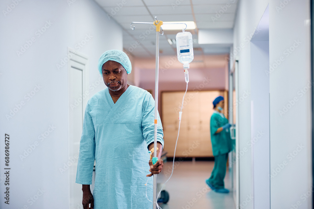 Black senior man with IV drip walking through hospital hallway. Black senior man with IV drip walking through hospital hallway.
