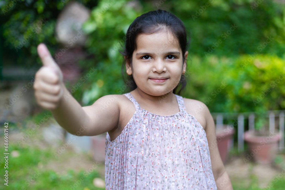 Beautiful Young Indian girl standing in public park showing thumbs up sign.
