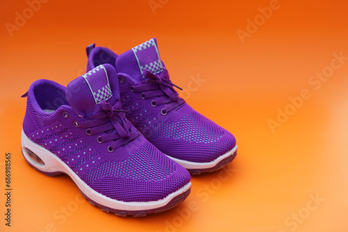 Pair of new purple sneakers. Fashionable and comfortable sport footwears. Orange background. Concept, shoes for doing sport or exercise also can wear for traveling, hiking.