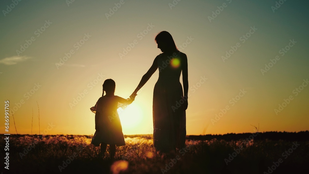Young mama walking in evening summer field with daughter with long braids