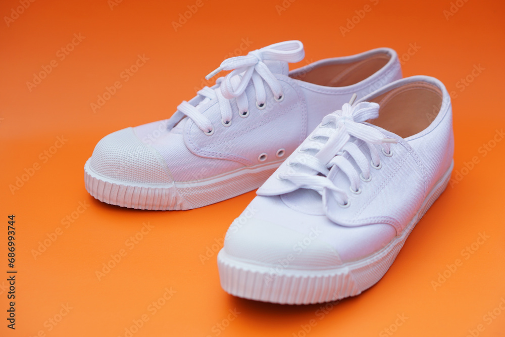 Pair of new white canvas sneakers,  Orange background. Comfortable, fashionable style. Concept, shoes for doing sport or exercise also can wear for traveling, hiking or doing active activity.