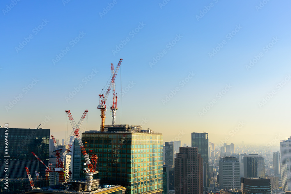 Tower cranes and unfinished buildings, construction cranes on blue sky with city skyscrapers background at construction site.