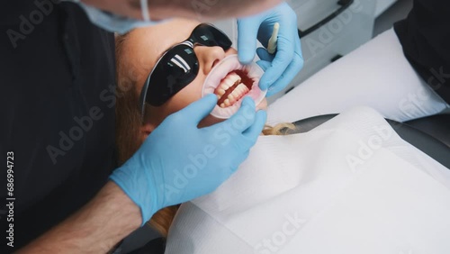 Close-up of dentist inserting dental cap into customer's mouth for treatment. Young woman wearing dental black glasses visiting orthodontist in hospital. photo