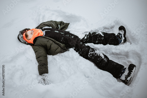 Boy laying in deep snow making snow angel photo