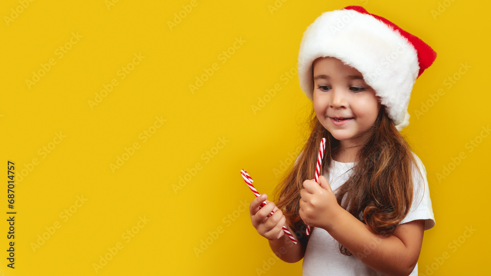 Portrait little girl child hold christmas candy cane enjoy want eat on new year party wear Santa hat isolated over yellow color background Portrait little girl child hold christmas candy cane enjoy want eat on new year party wear Santa hat isolated over yellow color background