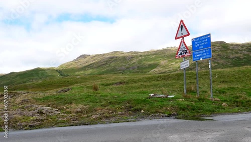 Steep ascent triangle warning road sign in Duddon Valley, white van or minibus driving up the narrow curvy road near Hardknott mountain pass in Lake District National Park, United Kingdom. photo